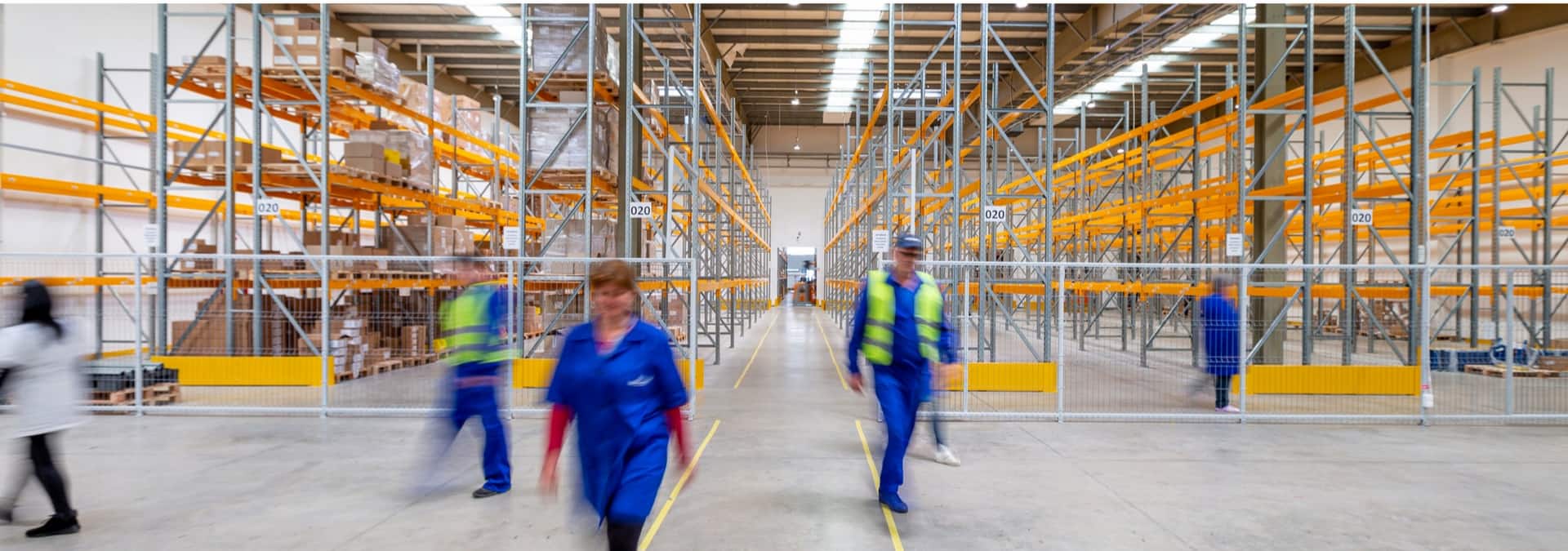 A imagem mostra cinco pessoas uniformizadas dentro de um grande estoque vazio, ilustrando a distribuição de produtos.